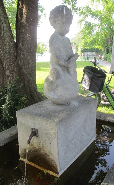 Ein Brunnen in M�nnedorf
                  (Schweiz)19.6.2024: Komischer Brunnen mit einer
                  kleinen Statue mit einem B�blein mit einem
                  "Fisch" in der Hand, und der Bub reitet